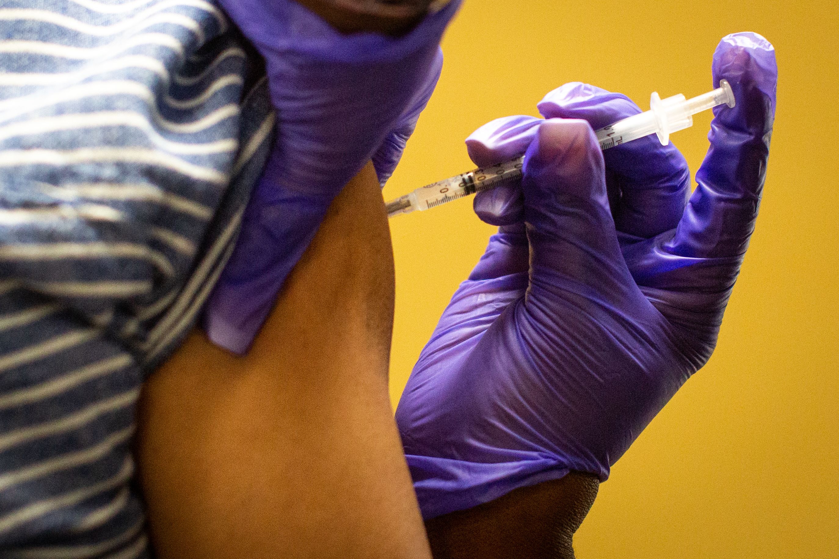 A gloved hand is seen administering a COVID-19 vaccine using a syringe into a patient's arm.