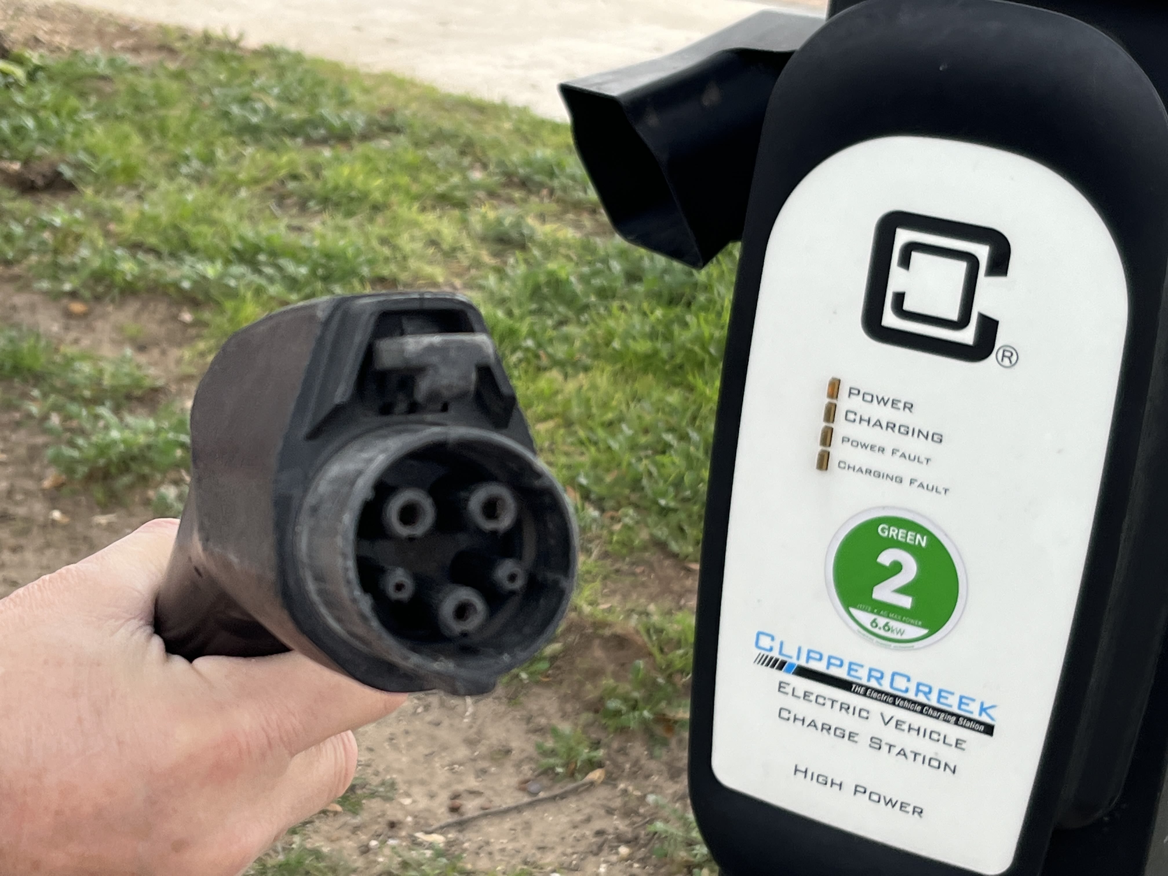A close-up of a level 2 electric vehicle charger. The end featuring the chargers prongs is seen and a sign in the back shows the charging level. It's labelled "ClipperCreek Electric Vehicle Charge Station."